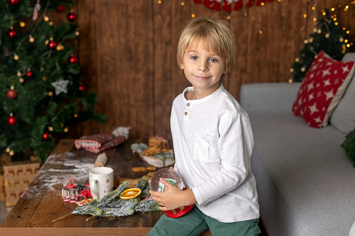 Beautiful blond child, young school boy, playing in a decorated home with knitted toys at Christmas