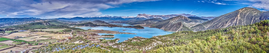 Drone panorama over the Mediano reservoir in the Spanish Pyrenees during the day in winter with snow-covered mountains in the background