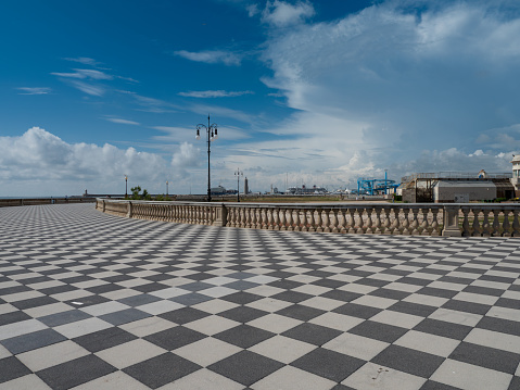 LIVORNO, ITALY - JUNE 5, 2023: The chequered black and white pavement of the Terrazza Mascagni in Livorno under a blue sky with scattered clouds