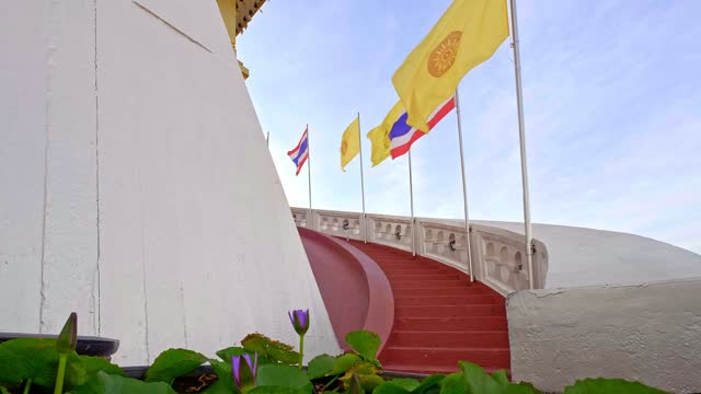 Thai national, buddhism and Thai Royal flags at red staircase and waterlilies at blue sunny sky.