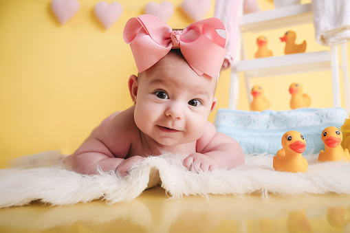 Adorable toddler girl kisses her newborn picture. The toddler is wearing pearls and a pink dress. Both of the girls are wearing a headband.