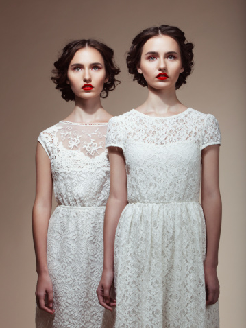 Studio portrait of two beautiful twins in white dresses. Professional make-up and hairstyle.