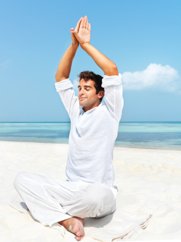 Happy young man performing yoga on a beautiful beach
