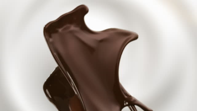 Liquid chocolate swirling and splashing on white milk background super slow motion