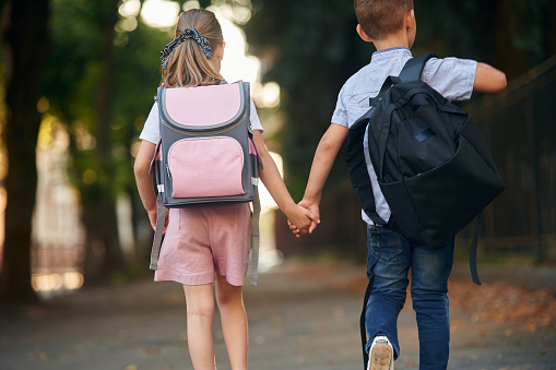 Back view, walking. Young school children of boy and girl are together outdoors.