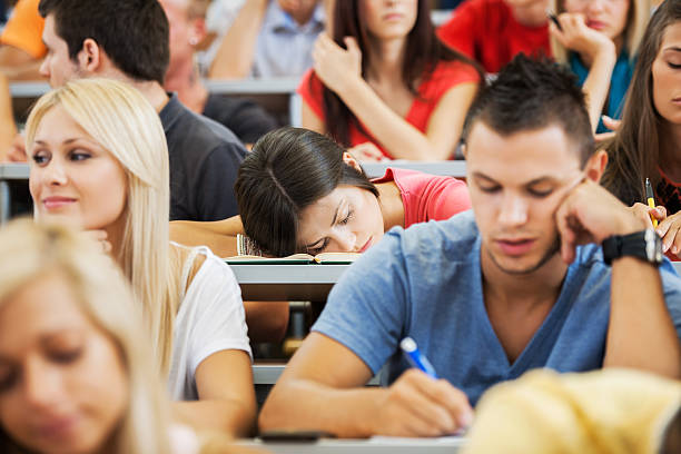 Young female student sleeping during a lecture. Large group of college students sitting in the university amphitheatre. The focus is on the woman sleeping. male college student sleeping through lecture stock pictures, royalty-free photos & images