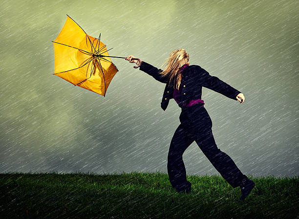 Wet, windy, winter weather blows woman and umbrella away "A young blonde woman hangs on helplessly to her yellow umbrella as it blows away from her, dragging her along in a wet,windy winter storm." gale stock pictures, royalty-free photos & images