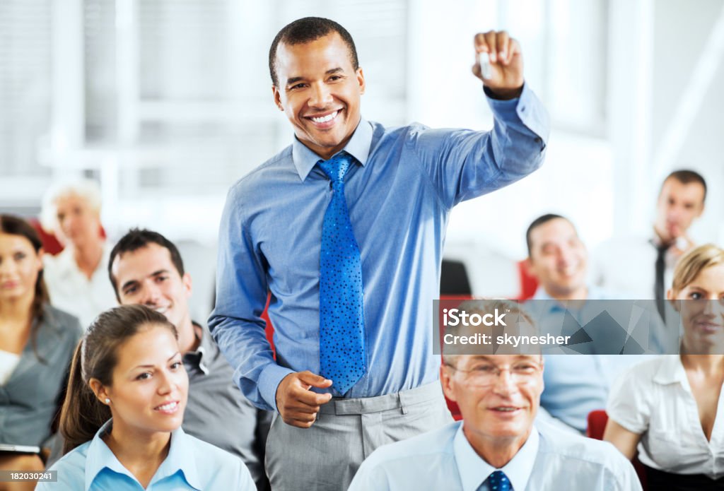 Group of businesspeople on a seminar "Cheerful businesspeople sitting and listening on a seminar, the focus is on African-American man standing and holding a pen." Audience Stock Photo