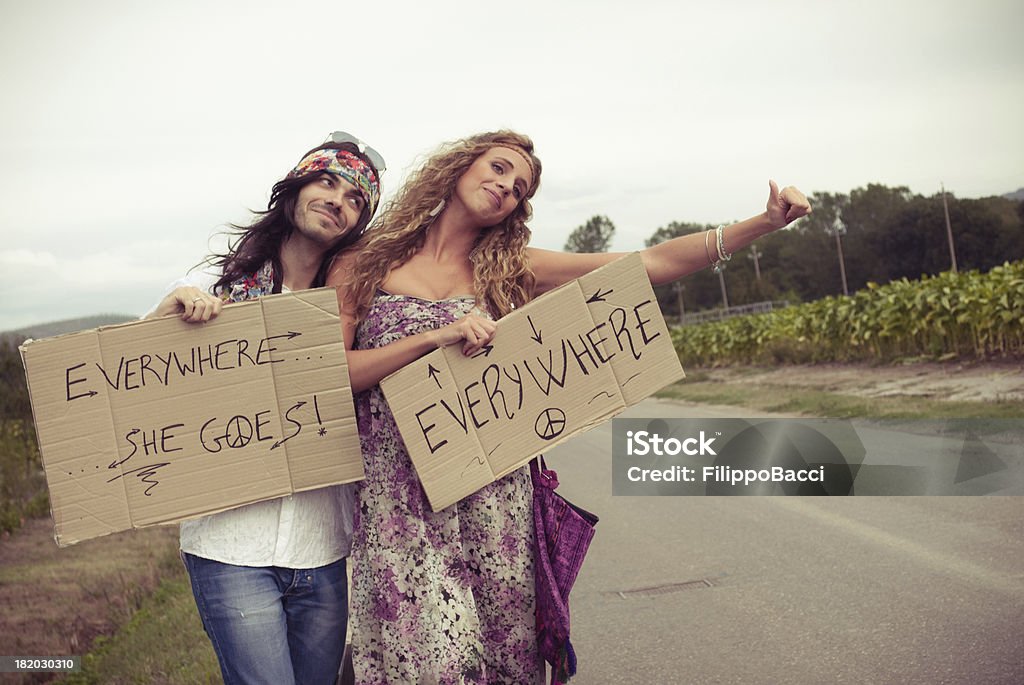 Young adult hippie couple hitchhiking with placards in hand Young adult hippie couple hitchhiking with placards in hand. Love concept. He's in love with her. 1960-1969 Stock Photo