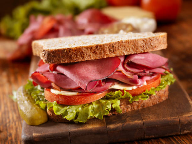 Pastrami Sandwich "Smoked Meat Sandwich with Lettuce, Tomato and Cheese on Whole Wheat Bread on a Cutting Board with all the Ingredients for Making it-Photographed on Hasselblad H3D2-39mb Camera" pastrami stock pictures, royalty-free photos & images