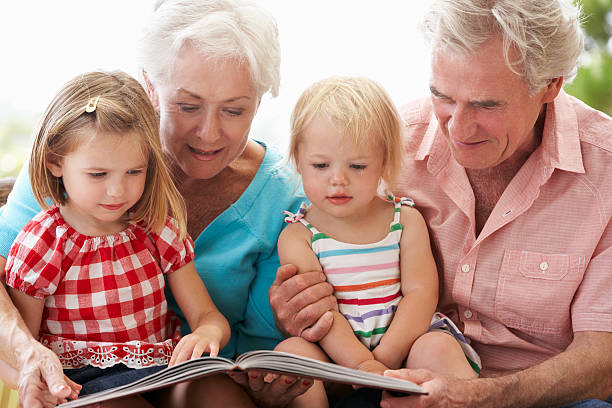 avós e netos a ler um livro no banco de jardim - grandparent reading grandmother child imagens e fotografias de stock