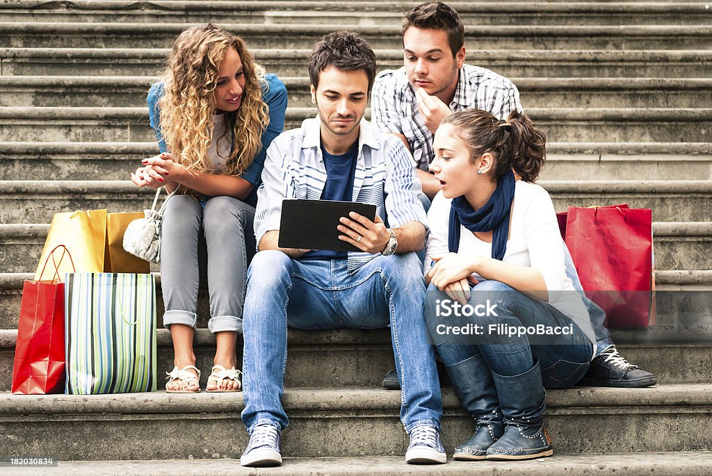 Quatro amigos usando um tablet sentado na escada - Foto de stock de 20-24 Anos royalty-free