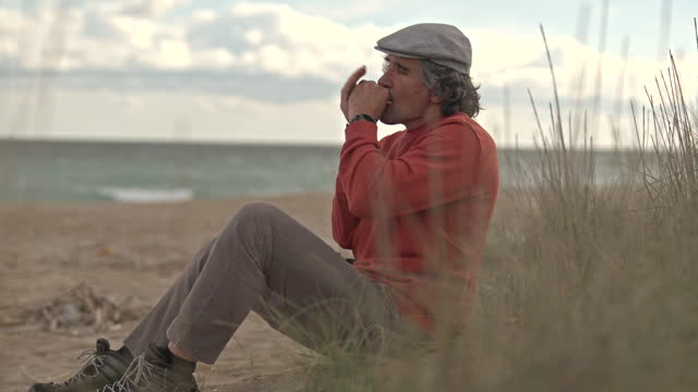 Man playing harmonica at the sea at sunset. Music in nature.