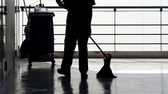 Silhouette image of cleaning service people sweeping the floor with a mop and other equipment on the trolley.