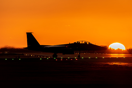 Silhouette of a military fighter jet aircraft entering the runway before take off in the sunset