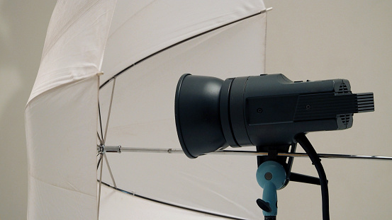 Big studio flashlight on a tripod and softbox paper in large size studio for video or film production. Film Light In Film Studio.
