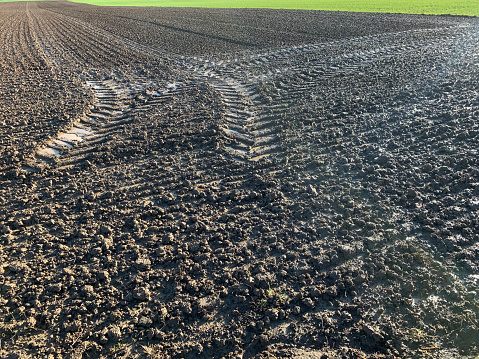 Plowed field with clods of soil wet after rain, close-up, tractor tracks, natural texture without horizon line, in Germany in sunny weather.