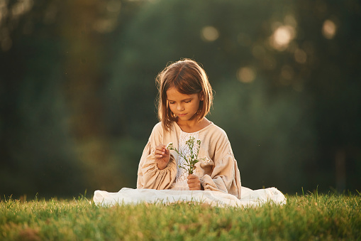 With small flowers in hands. Little girl is on the summer field outdoors.