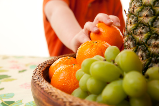 A 5 year old boy eating oranges from a healthy fruit basket.