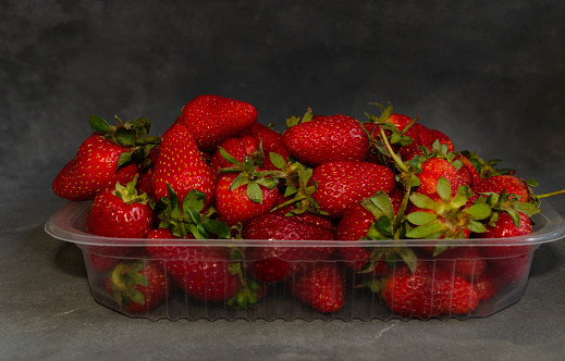 fresh red berries in plastic tray on gray background