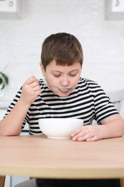 istock Little boy eating breakfast at wooden table in light white kitchen. 1820342367