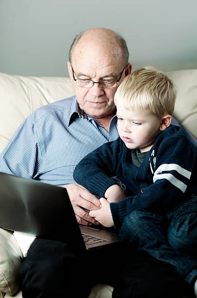 avô e neto olhar para laptop - generation gap multi generation family vertical holding hands - fotografias e filmes do acervo