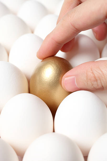 istock Hand Touching Gold Egg from a Crowd of Ordinary Eggs 182035476