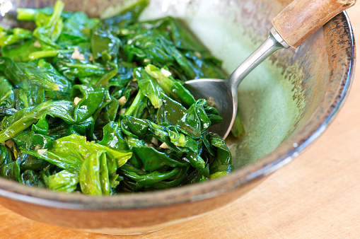 Pottery bowl of fresh sauteed spinach with garlic and wood-handled spoon