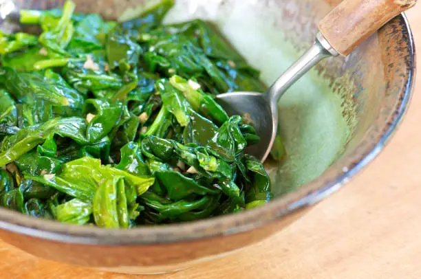 Pottery bowl of fresh sauteed spinach with garlic and wood-handled spoon