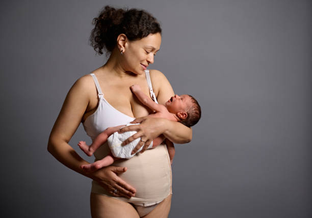 szczęśliwa mama w bieliźnie i bandażu elastycznym na brzuchu po cesarskim cięciu, uśmiechnięta patrząc na swoje nowo narodzone dziecko - cesarka zdjęcia i obrazy z banku zdjęć