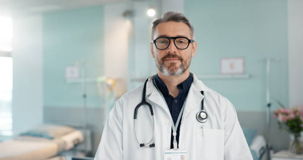 Healthcare, doctor and man with arms crossed at hospital with smile for support, service and wellness. Medicine, professional and expert with glasses and pride for career, surgery, insurance and care stock photo