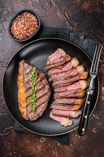 Sliced grilled medium rare Top sirloin beef steak on a plate. Dark background. Top view.