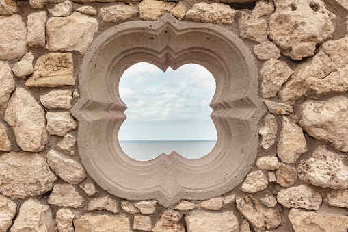 Round type window. Medieval flower shape hole window in rustic stone wall with ocean and sky behind