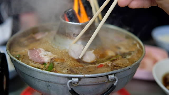 Slow motion of man put meatball into hot soup boiling. Thai fire hot pot with boiled braised beef soup