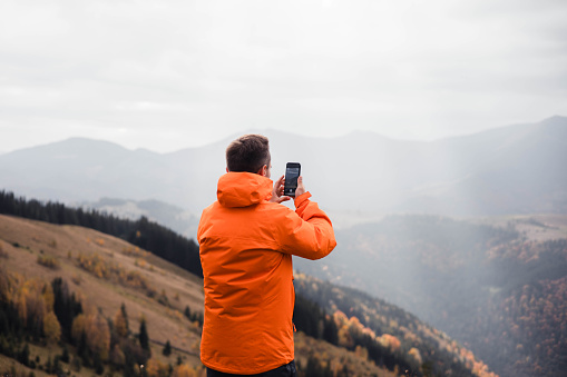 Shot of a young man taking pictures with his cellphone outdoors in the mountains Carpathian Mountains, Ukraine