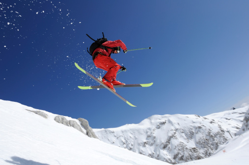 Side view of young male free ride skier in mid-air against the blue sky