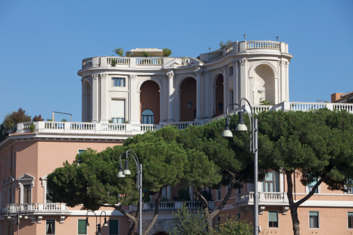 A beautiful Roman classical building by the Tiber river with unique terraces and surrounded by trees.