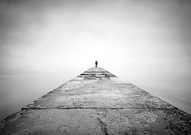 Man on the edge of pier "Man is thinking on the edge of pier. Image was shot with long exposure, therefore water looks in this way. Only man was pasted and horizon was removed, other on the photo is original. Man was pasted from another image" silhouette of depressing stock pictures, royalty-free photos & images