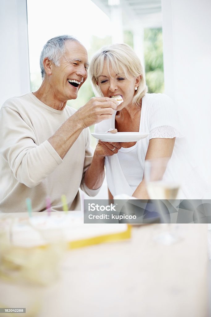 Cheerful senior man feeding mature woman a piece of cake Portrait of cheerful senior man feeding mature woman a piece of cake Eating Stock Photo