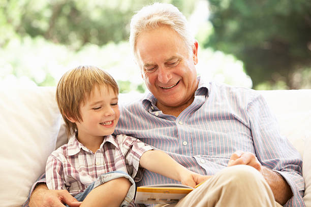 abuelo con nieto lectura en sofá - grandson fotografías e imágenes de stock