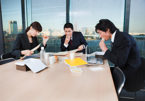Subject: Three Japanese office workers working together in a panic over lunch meeting for work deadline in a conference room.Location: Tokyo Japan.
