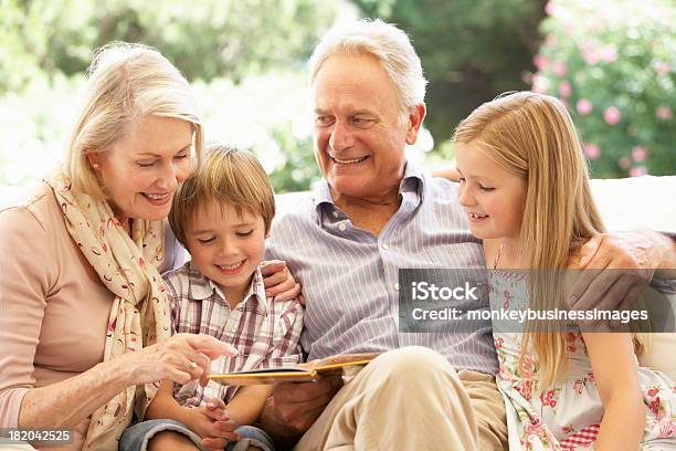 Portrait Of Grandparents Reading To Grandchildren On Sofa Stock Photo - Download Image Now