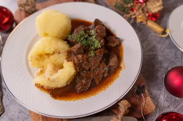 Delicious christmas meat dish with braised beef goulash and potato dumplings in a delicious brown sauce on a plate with christmas decoration.