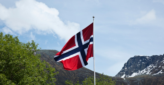 Norwegian flag. Background of mountains and green trees in spring.