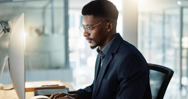 istock Thinking, businessman and reading on computer with a smile in office for email, feedback or communication. Working, online or black man with research, inspiration or ideas from Nigeria report or news 1820432494