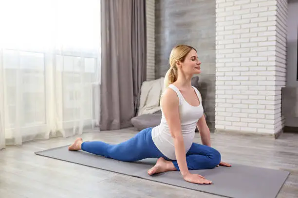 sportive mom-to-be stretching legs during workout at home, flexible strong lady in leggins and t-shirt preparing for yoga training, warm up body muscles