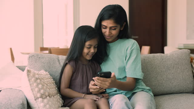 Indian mom spend time with daughter using together modern smartphone