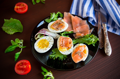 boiled eggs with salted red fish, herbs and seasonings in a plate on a wooden table.