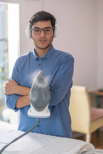 Young handsome man ironing laundry at home.