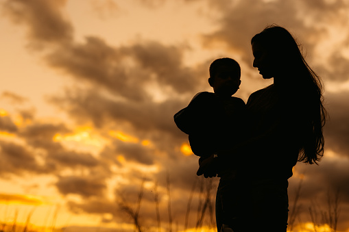 Silhouette of a beautiful young mother holding her son in her arms in the park in autumn.